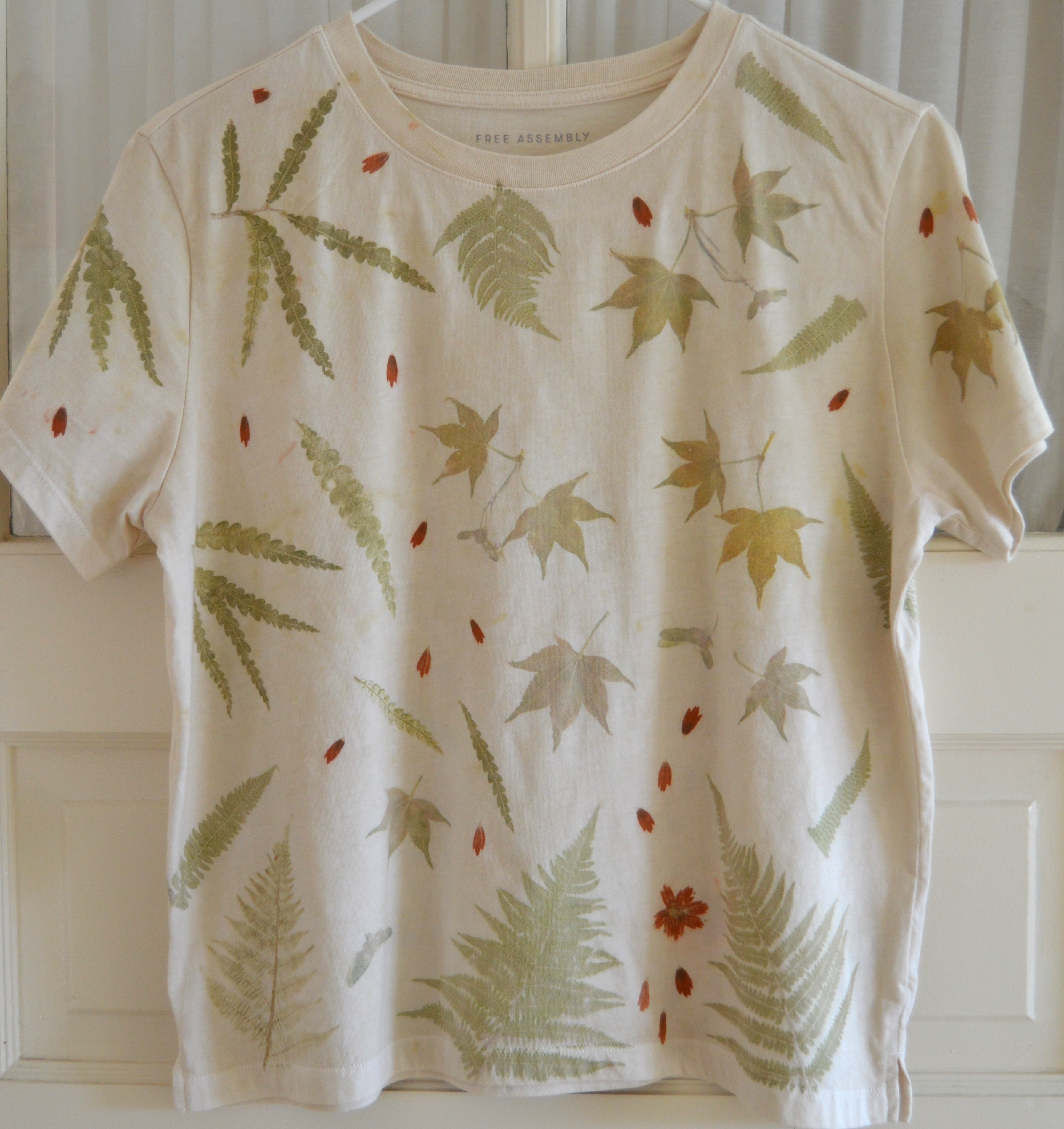 Front of a cream combed-cotton T-shirt pounded with late-summer ferns, maple leaves, and small red blooms