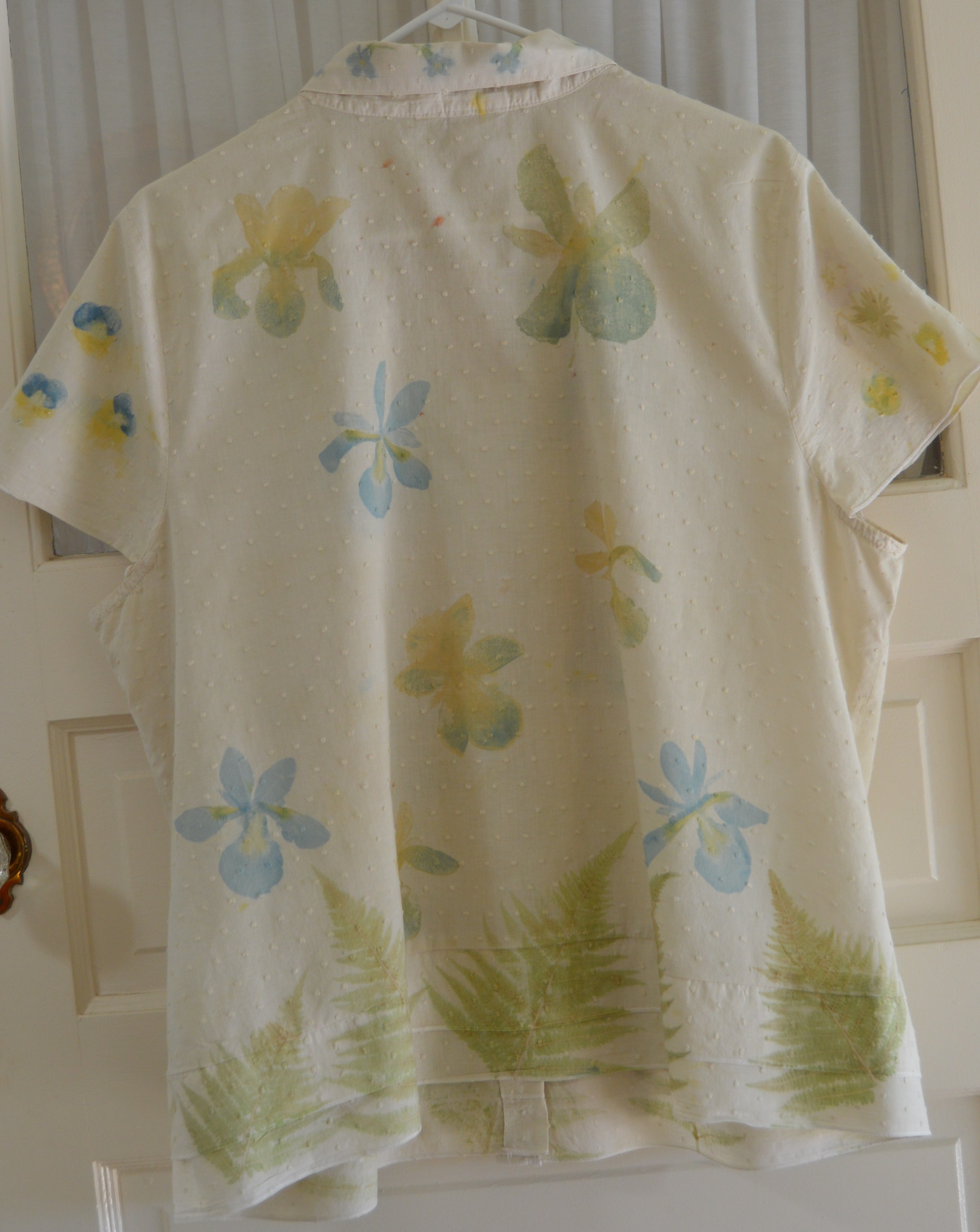 Back of a cream Swiss dot cotton blouse with blue and yellow iris and green fern motifs mirrored from the front