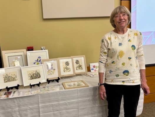 The artist wearing a spring-flower pounded long-sleeve shirt at a workshop, with framed mirror-creations displayed behind her